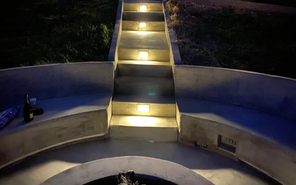 Custom Concrete steps with built-in lighting leading to a circular fire pit seating area at night in Knoxville, Tennessee.