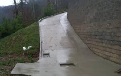 Concrete driveway in Sevierville with curb, flume, and drainage system installed for proper water runoff near a retaining wall.